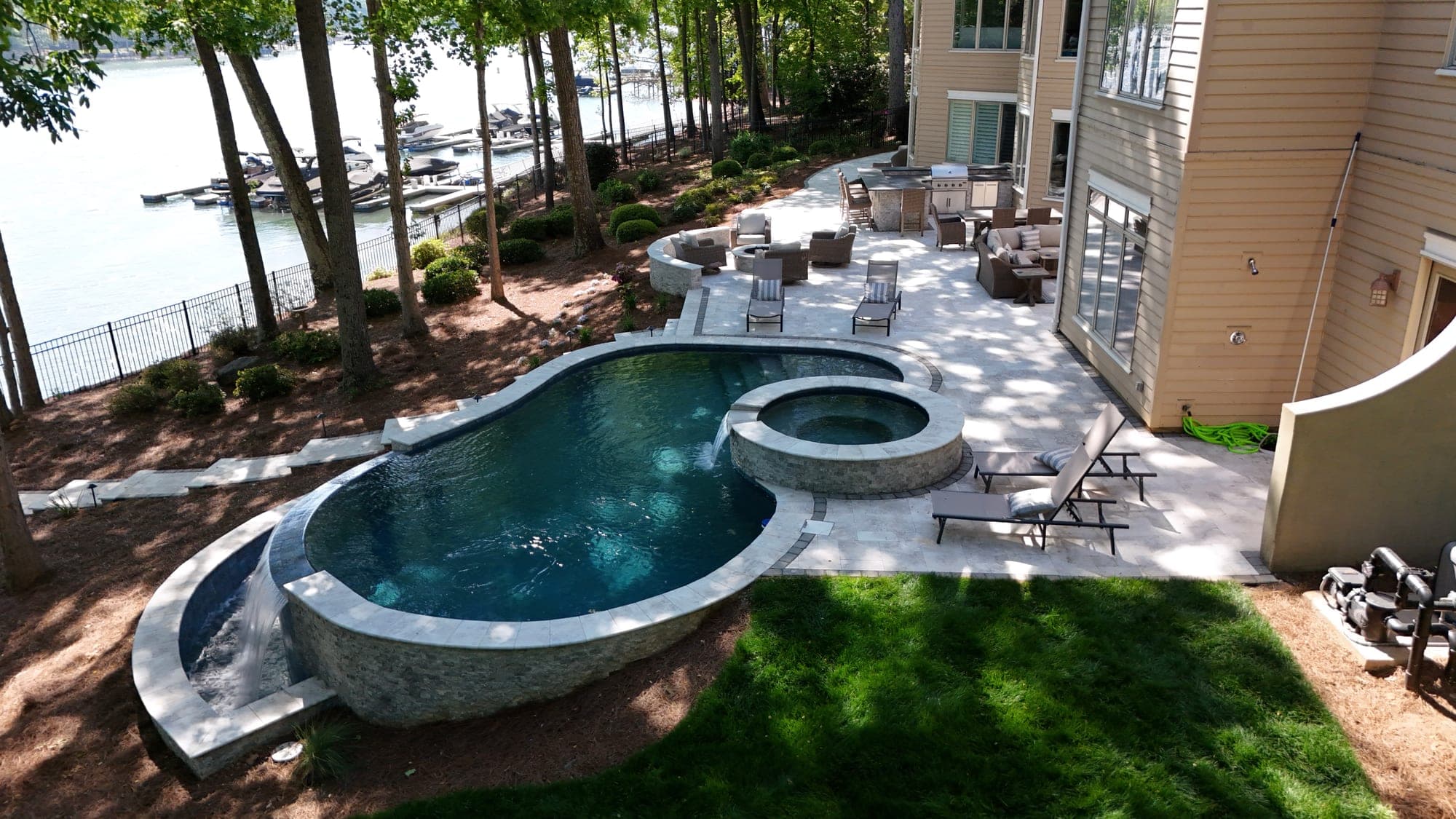 Aerial drone photo of a lakefront luxury home with an infinity pool, stone patio, and private dock